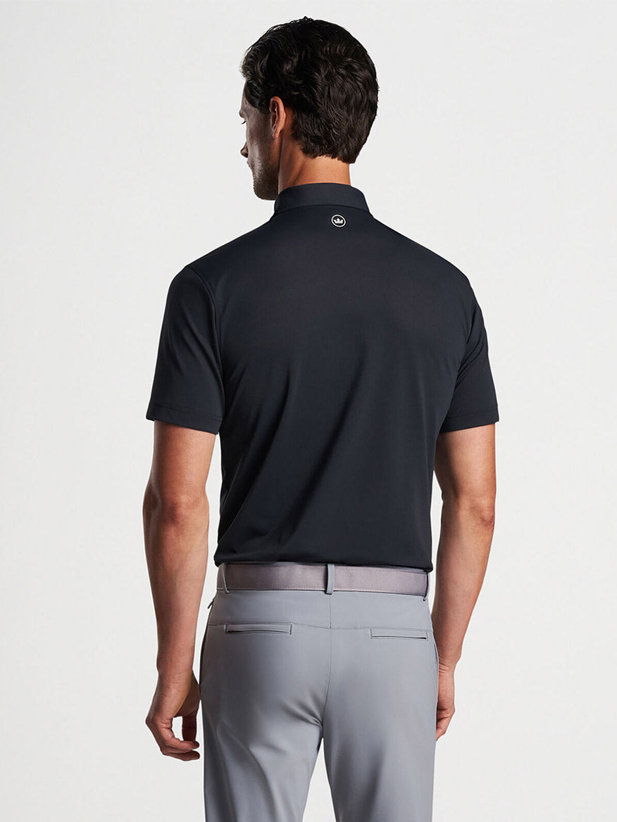 Man wearing a Peter Millar Soul Performance Mesh Polo in Black and grey trousers seen from behind.