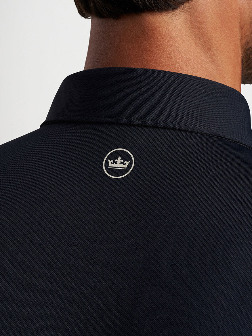 A man from behind showing the collar of a Peter Millar Soul Performance Mesh Polo in Black shirt with a small logo featuring a crown.
