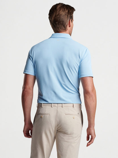 Man wearing a Peter Millar Soul Performance Mesh Polo in Blue Frost and beige trousers viewed from the back.