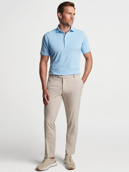 Man posing in a Peter Millar Soul Performance Mesh Polo in Blue Frost and beige trousers with white shoes.