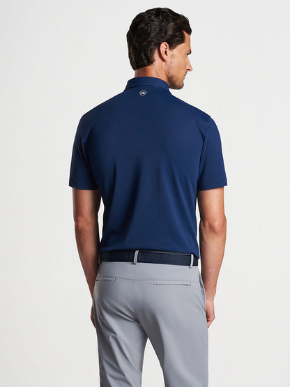 A man viewed from behind wearing a Peter Millar Soul Performance Mesh Polo in Navy and light grey trousers.