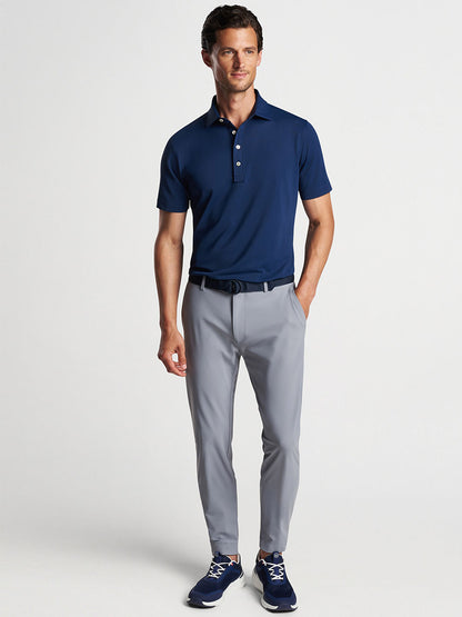 A man wearing a Peter Millar Soul Performance Mesh Polo in Navy, gray trousers, and navy blue sneakers stands against a neutral background.