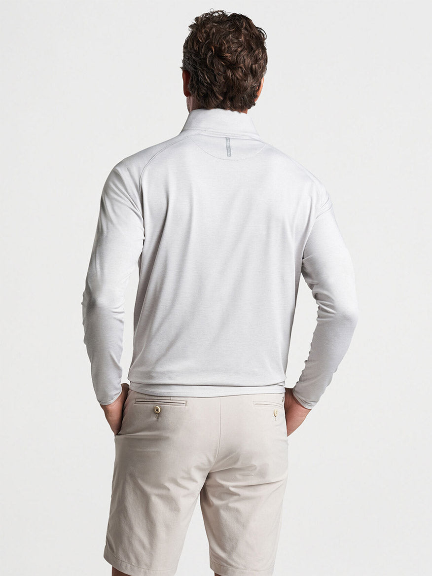 A man viewed from behind wearing a Peter Millar Stealth Performance Quarter-Zip in British Grey made of wicking fabric and beige shorts.