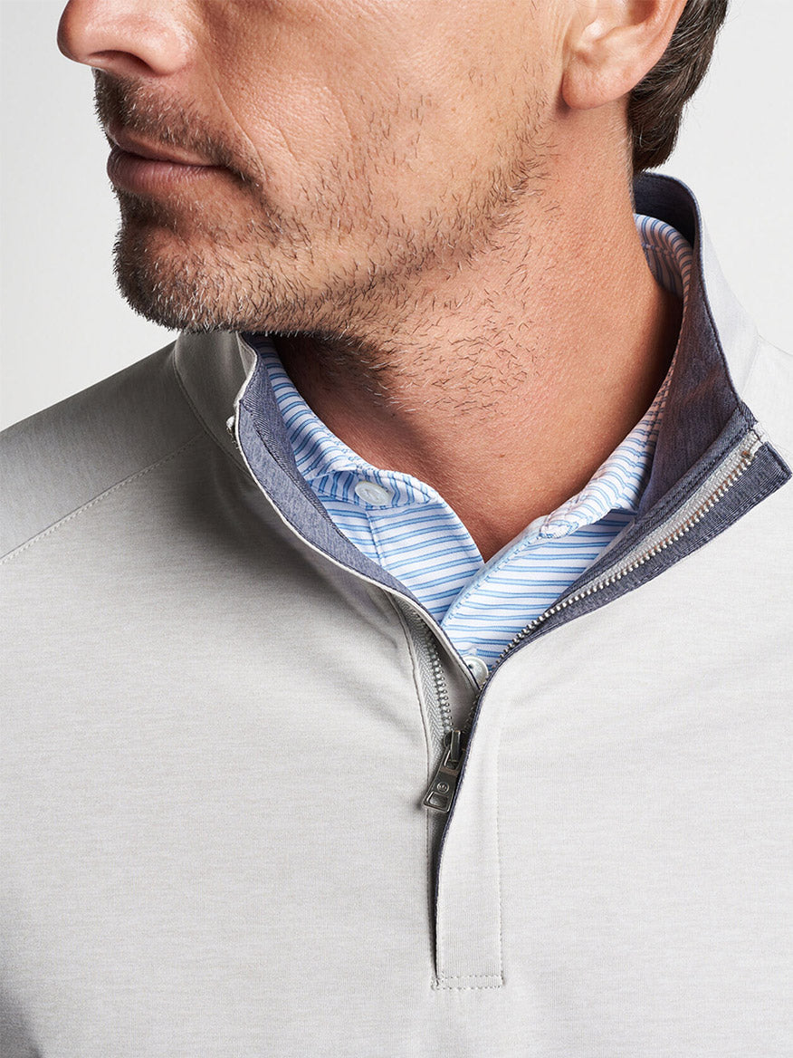 Close-up of a man wearing a Peter Millar Stealth Performance Quarter-Zip in British Grey over a collared, striped shirt made of UPF 50+ wicking fabric.
