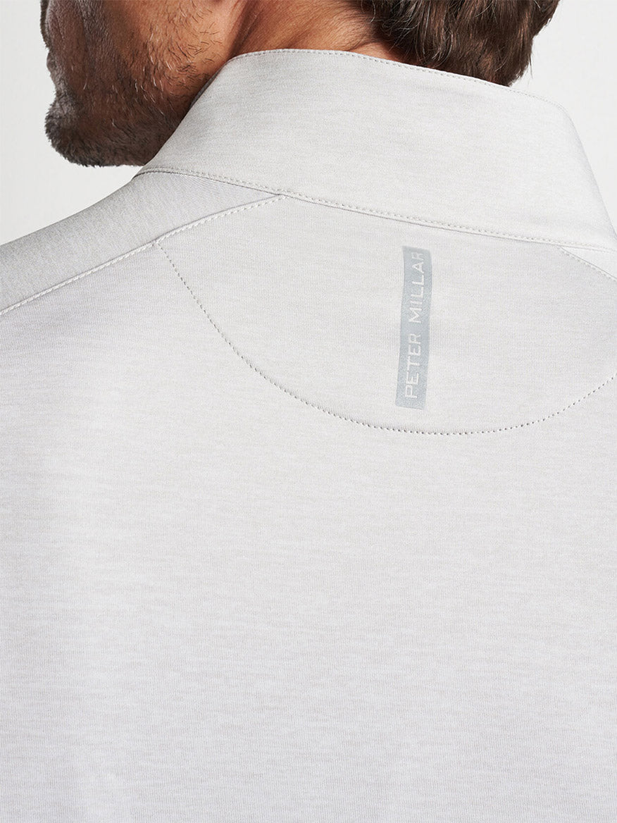 Close-up of the back of a man's shirt collar displaying a "Peter Millar Stealth Performance Quarter-Zip in British Grey" label with UPF 50+ protection.