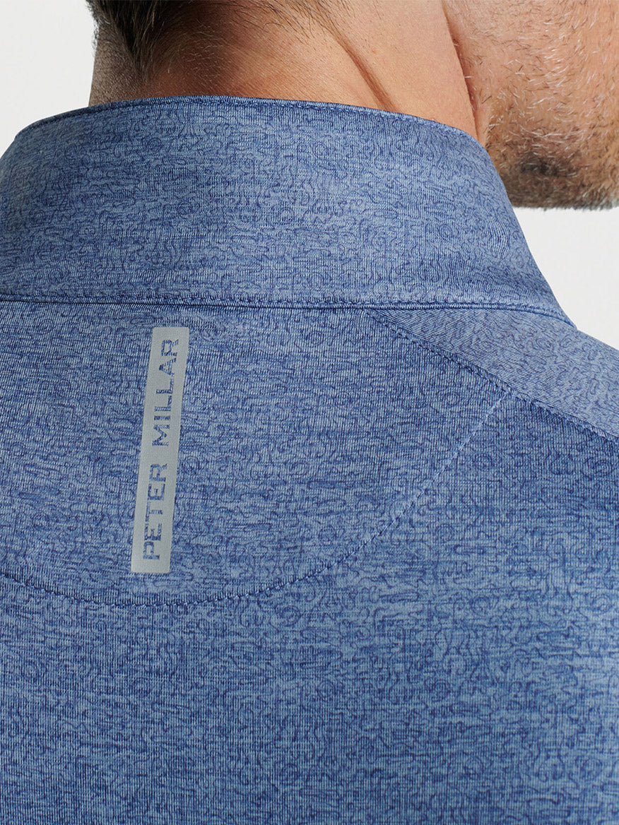 Close-up of the back collar of a blue textured Peter Millar Stealth Performance Quarter-Zip in Blue Pearl with a "peter millar" label.