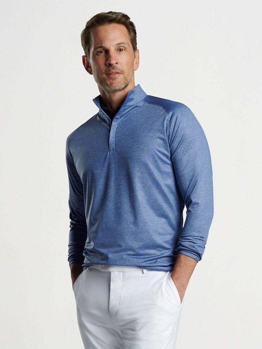 Man posing in a Peter Millar Stealth Performance Quarter-Zip in Blue Pearl with UPF 50+ sun protection and white trousers.
