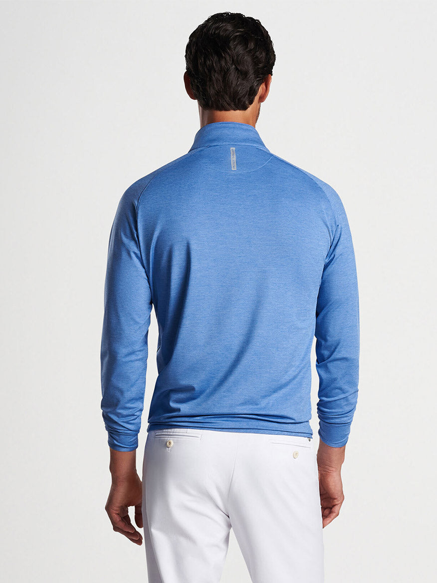 Man wearing a Peter Millar Stealth Performance Quarter-Zip in Cascade Blue with UPF 50+ sun protection and white pants viewed from the back.