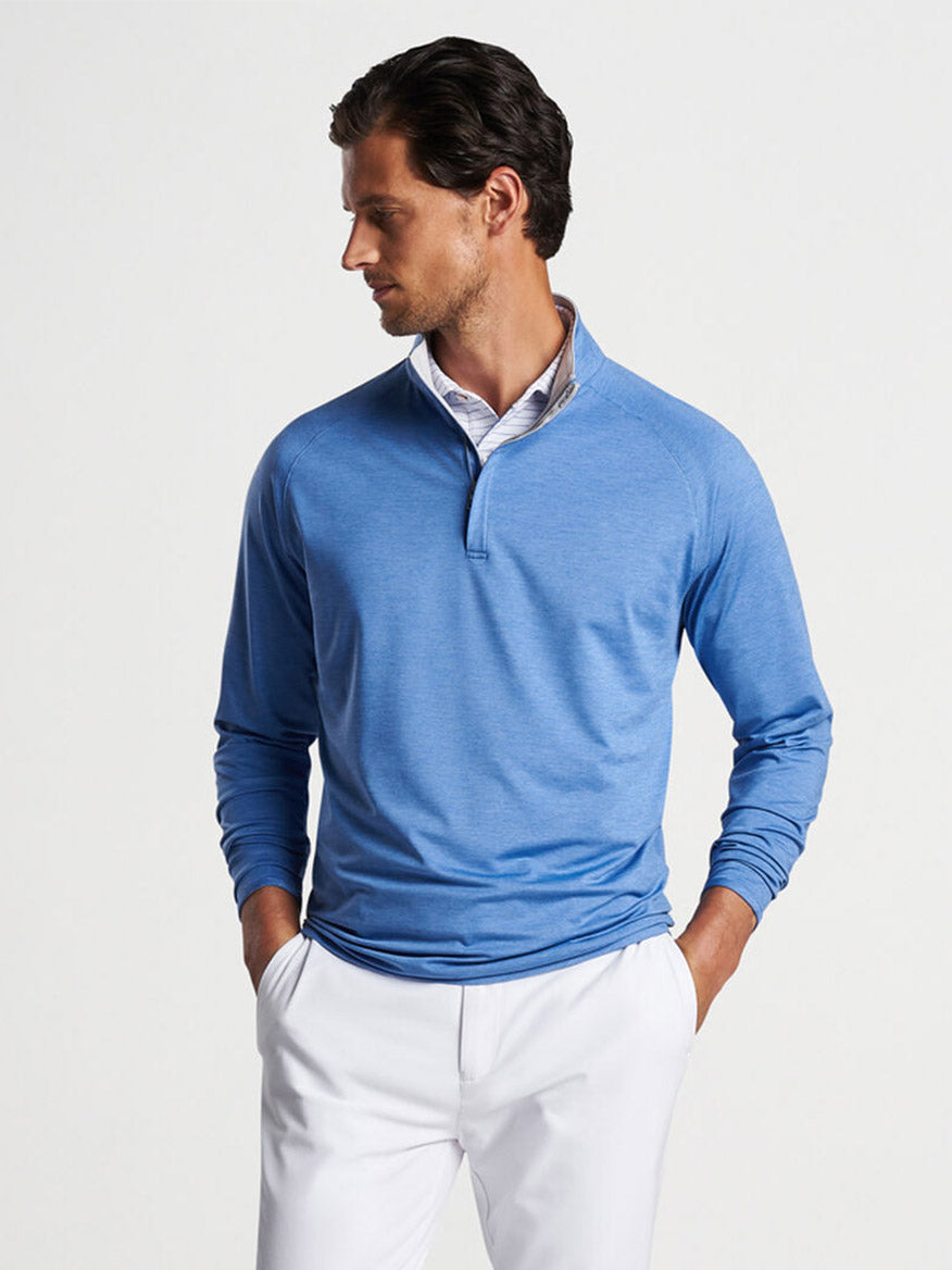 A man wearing a Peter Millar Stealth Performance Quarter-Zip in Cascade Blue with UPF 50+ sun protection and white pants looking to the side.