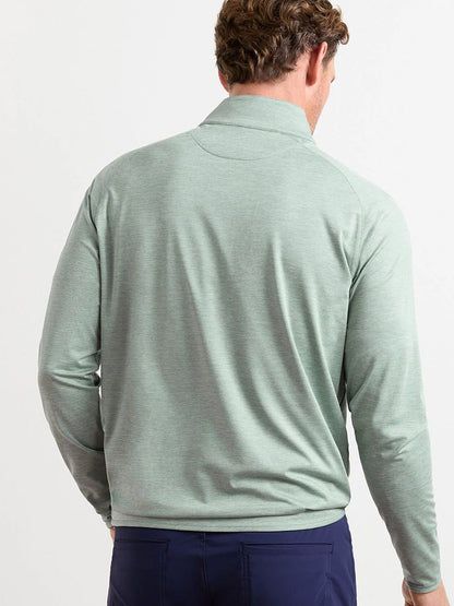 A man with short, curly hair is seen from behind wearing the Peter Millar Stealth Performance Quarter-Zip in Willow and dark blue pants against a plain background.