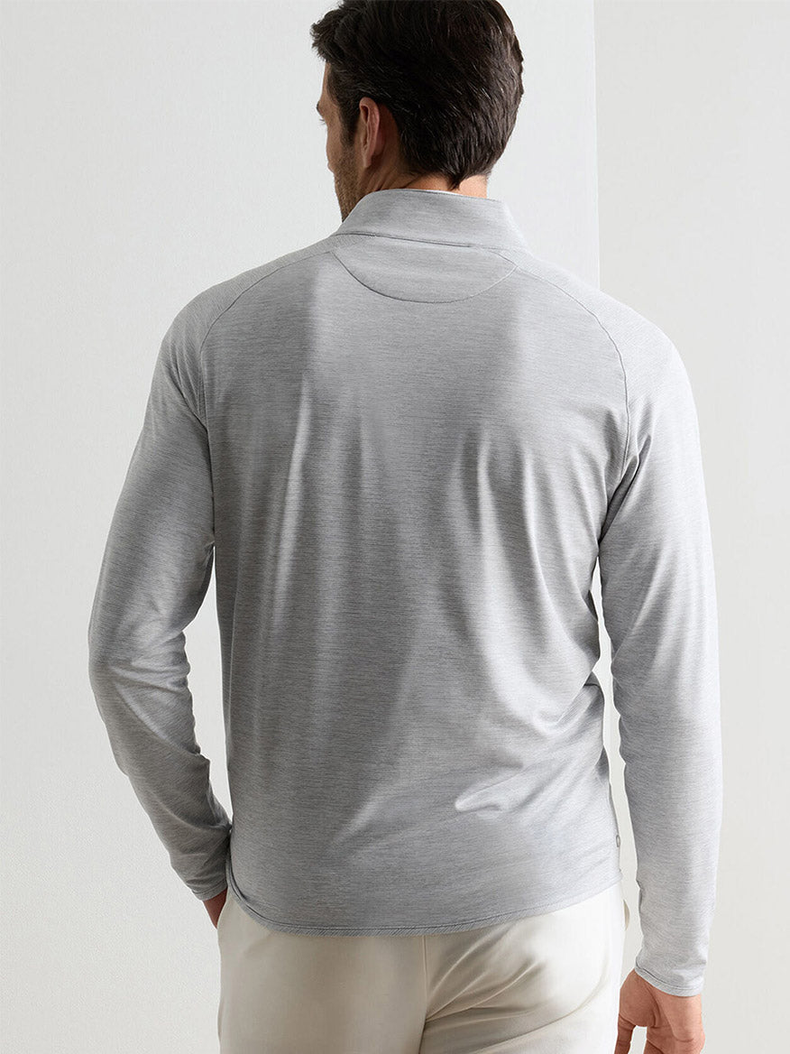 A man faces away, wearing the Peter Millar Stealth Stripe Performance Quarter-Zip in Gale Grey, featuring moisture-wicking fabric, paired with beige pants against a plain light background.