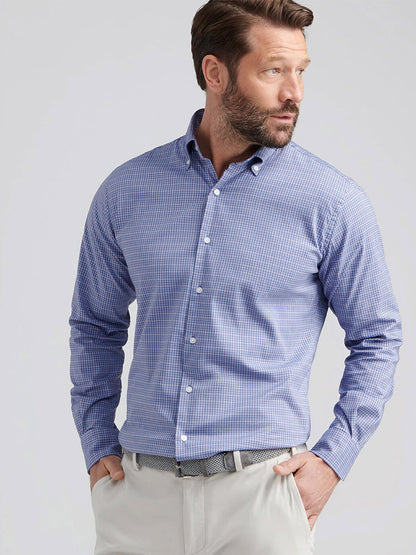 A man wearing the Peter Millar Stowe Crown Lite Cotton-Stretch Sport Shirt in Deep Violet and light-colored pants looks to the side with one hand in his pocket.