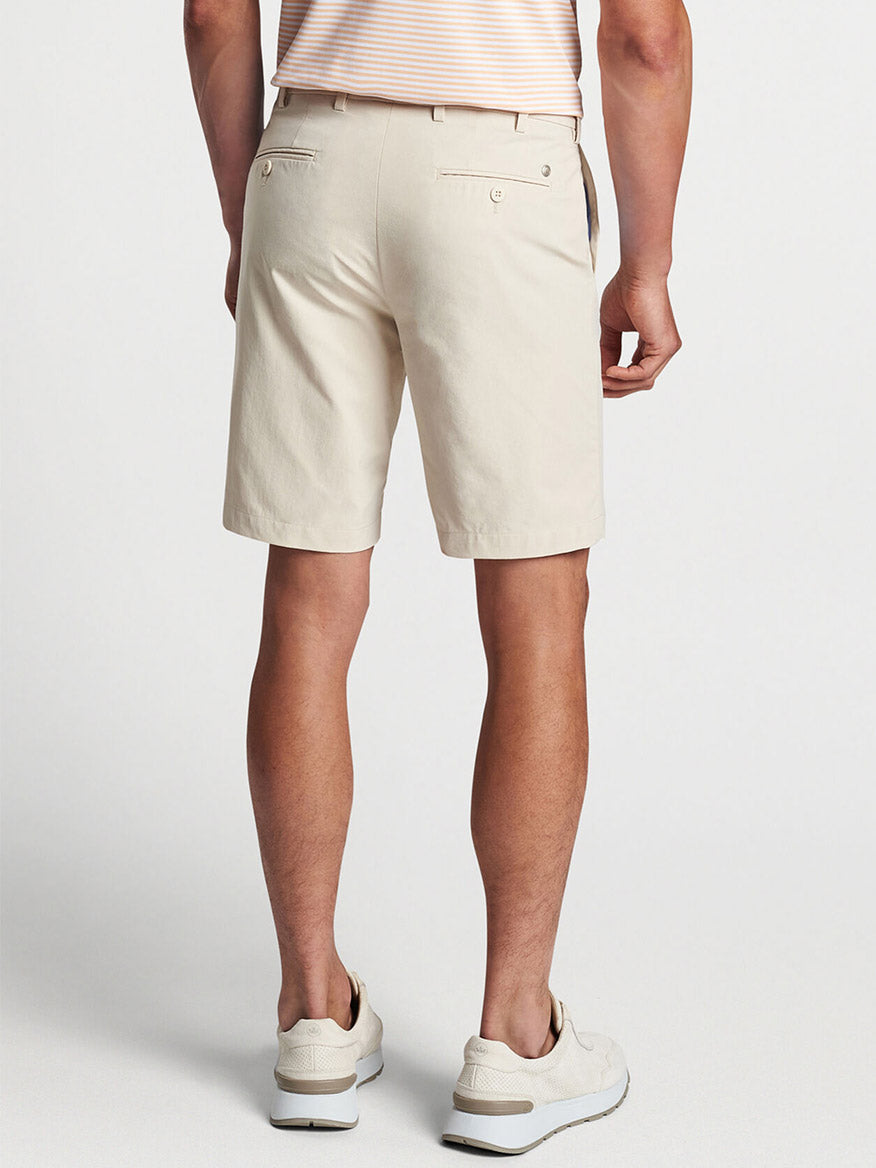 Man wearing Peter Millar Surge Performance Short in British Cream and white sneakers standing against a neutral background.