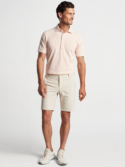 Man posing in a casual outfit with a striped polo shirt featuring four-way stretch, Peter Millar Surge Performance Short in British Cream, and white sneakers.