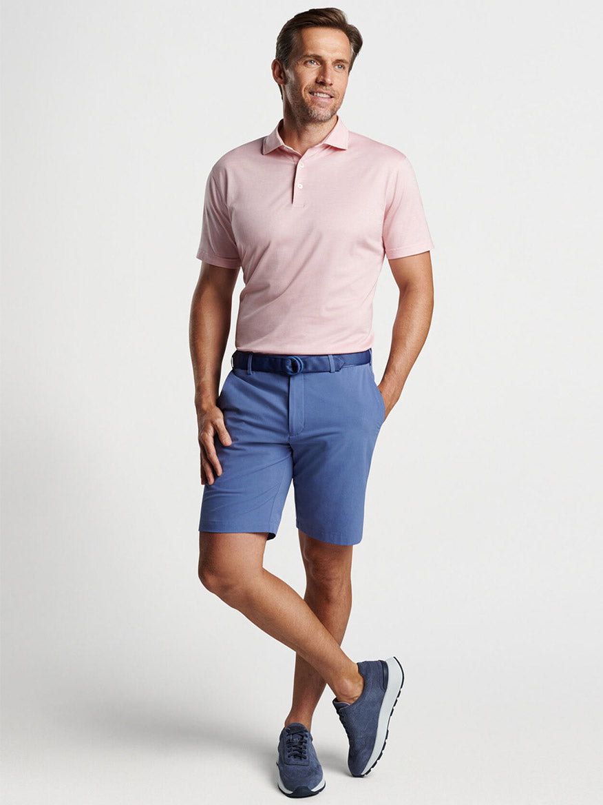 Man posing in a pink polo shirt and Peter Millar Surge Performance Short in Blue Pearl shorts.