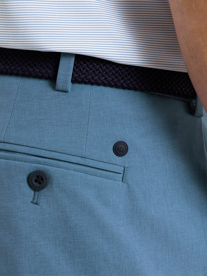 Close-up of a person wearing the Peter Millar Surge Performance Short in Storm, featuring four-way stretch and a back pocket, styled with a dark braided belt and a white shirt with thin horizontal stripes.