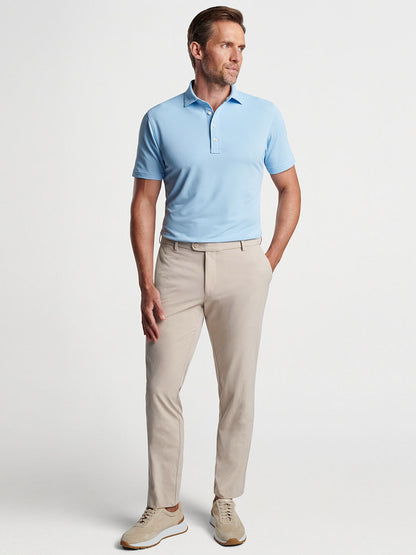 Man in a light blue polo shirt and Peter Millar Surge Performance Trouser in Oatmeal standing against a neutral background.