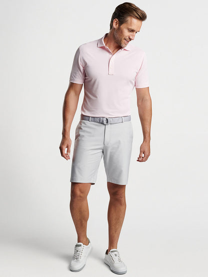 A man in a pink polo shirt with four-way stretch and Peter Millar Surge Signature Performance Short in British Grey looking down to his side against a plain background.