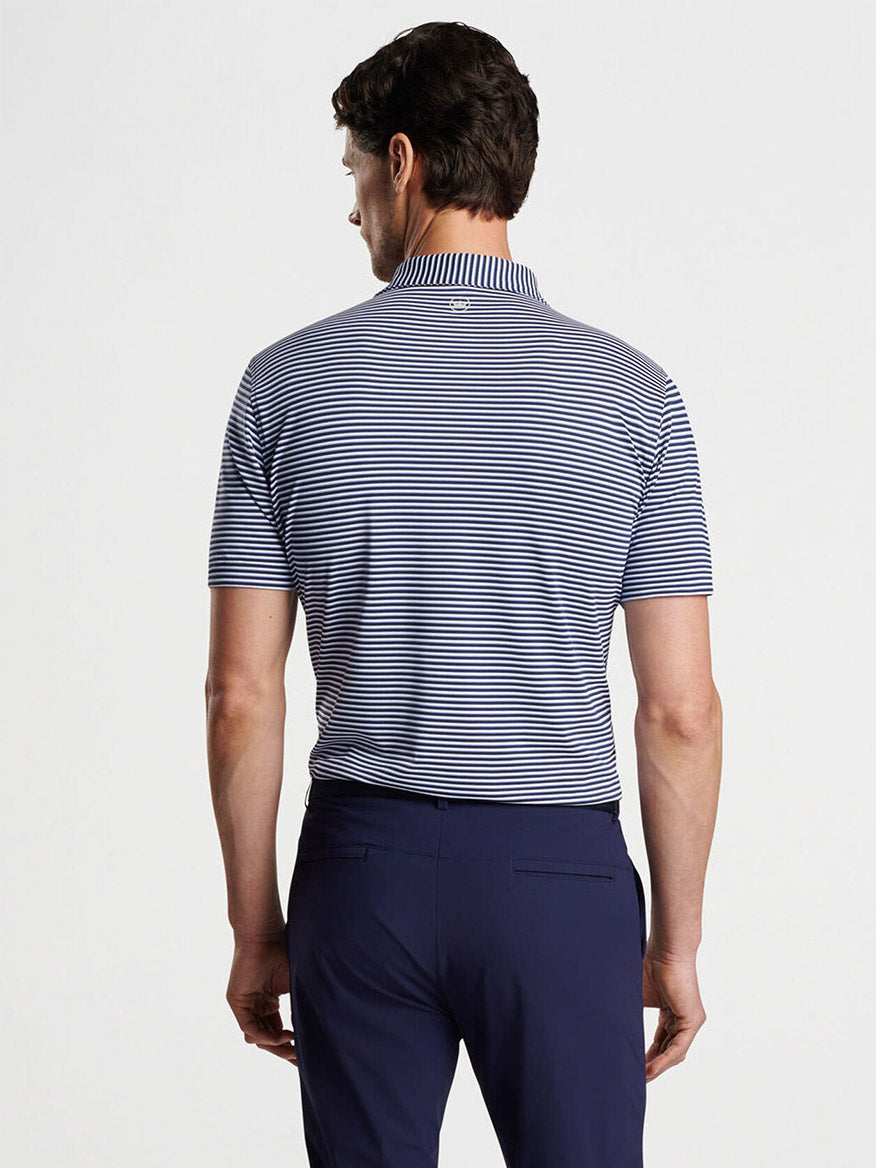 A person is wearing a Peter Millar Tempo Performance Mesh Polo in Navy with a vintage-inspired collar, along with navy pants, standing and facing away.