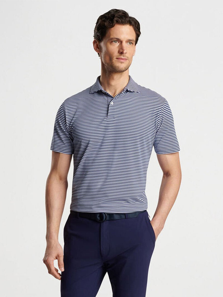 A man wearing a Peter Millar Tempo Performance Mesh Polo in Navy and dark pants stands looking to the side against a plain background.