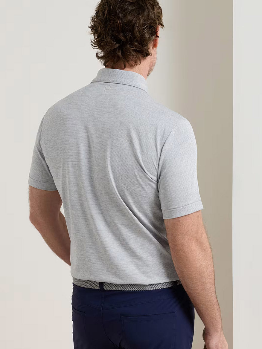 A man wearing the Peter Millar Treble Performance Jersey Polo Edwin Spread Collar in Gale Grey and dark blue pants stands with his back to the camera.