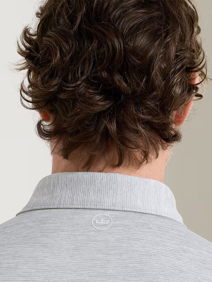 A person with curly brown hair is seen from behind, wearing the Peter Millar Treble Performance Jersey Polo Edwin Spread Collar in Gale Grey, featuring four-way stretch and a small logo below the collar.
