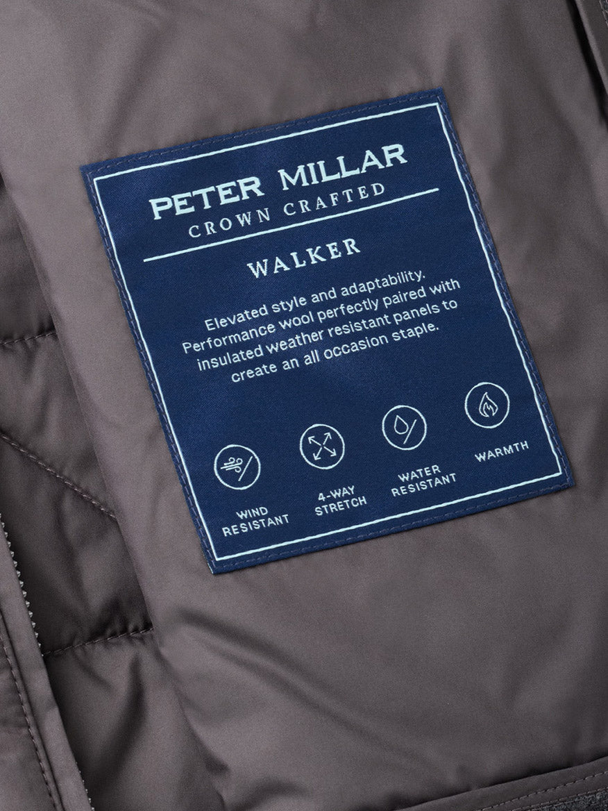 Close-up of the Peter Millar Walker Hybrid Jacket in Iridium label, highlighting features such as wind resistance, 4-way stretch, water resistance, and warmth, with descriptive text on a navy patch.