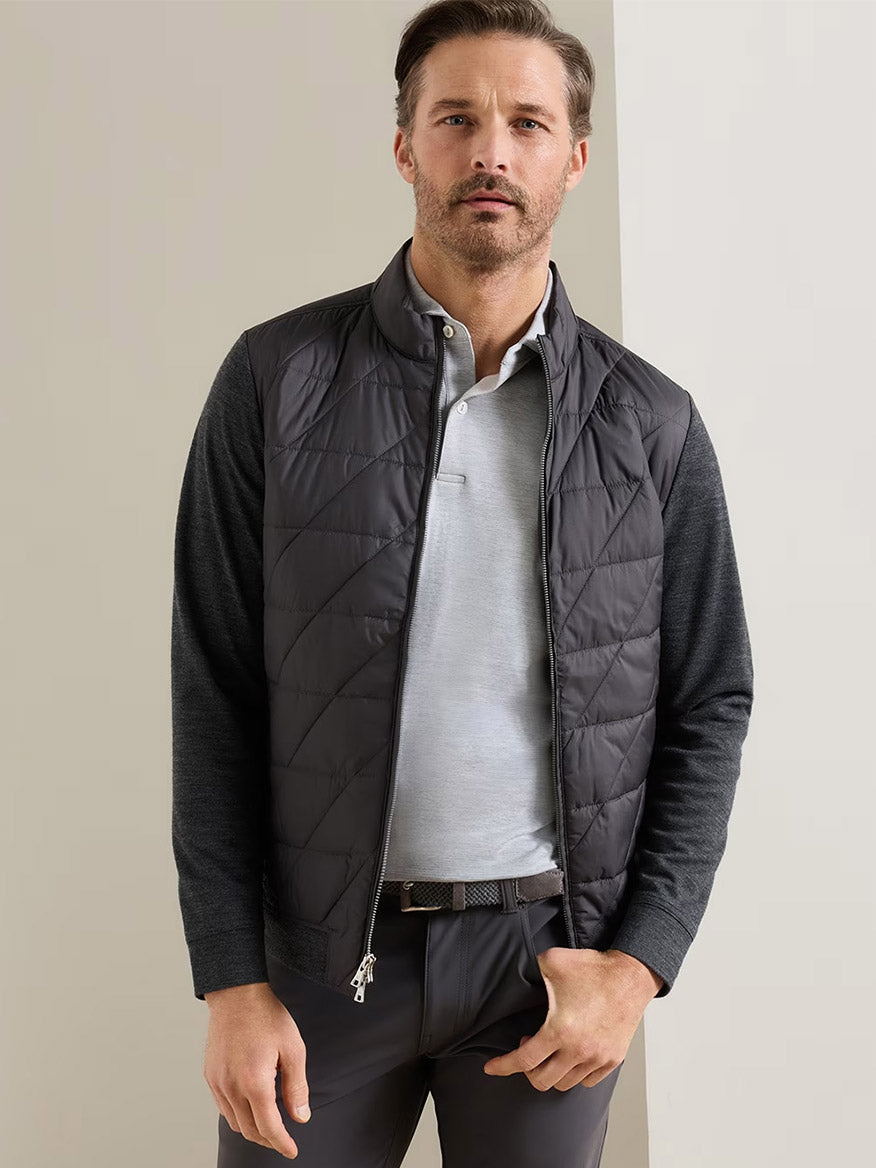 A man wearing a light gray polo, dark pants, and the Peter Millar Walker Hybrid Jacket in Iridium stands against a plain light background.