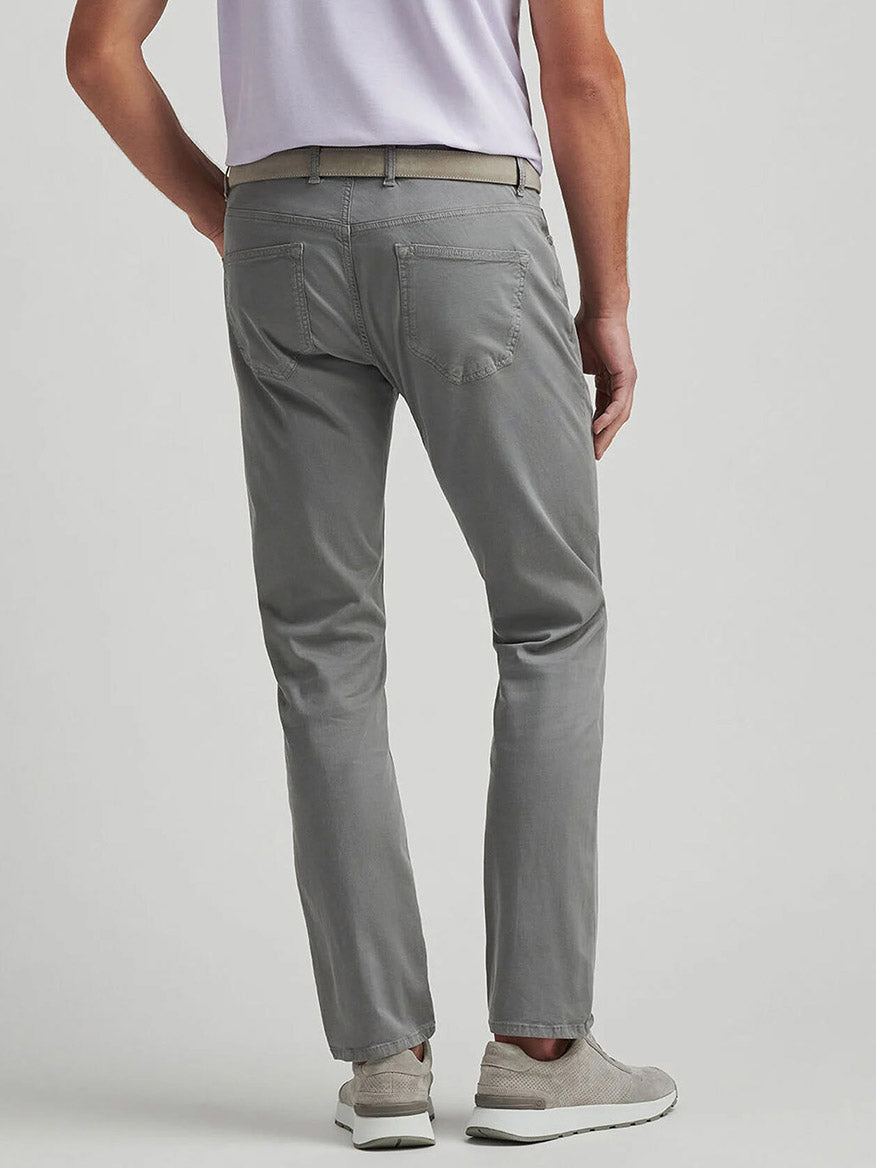 A person is seen from the back wearing Peter Millar Wayfare Five-Pocket Pant in Classic Grey, a light belt, white sneakers, and a short-sleeved white shirt.