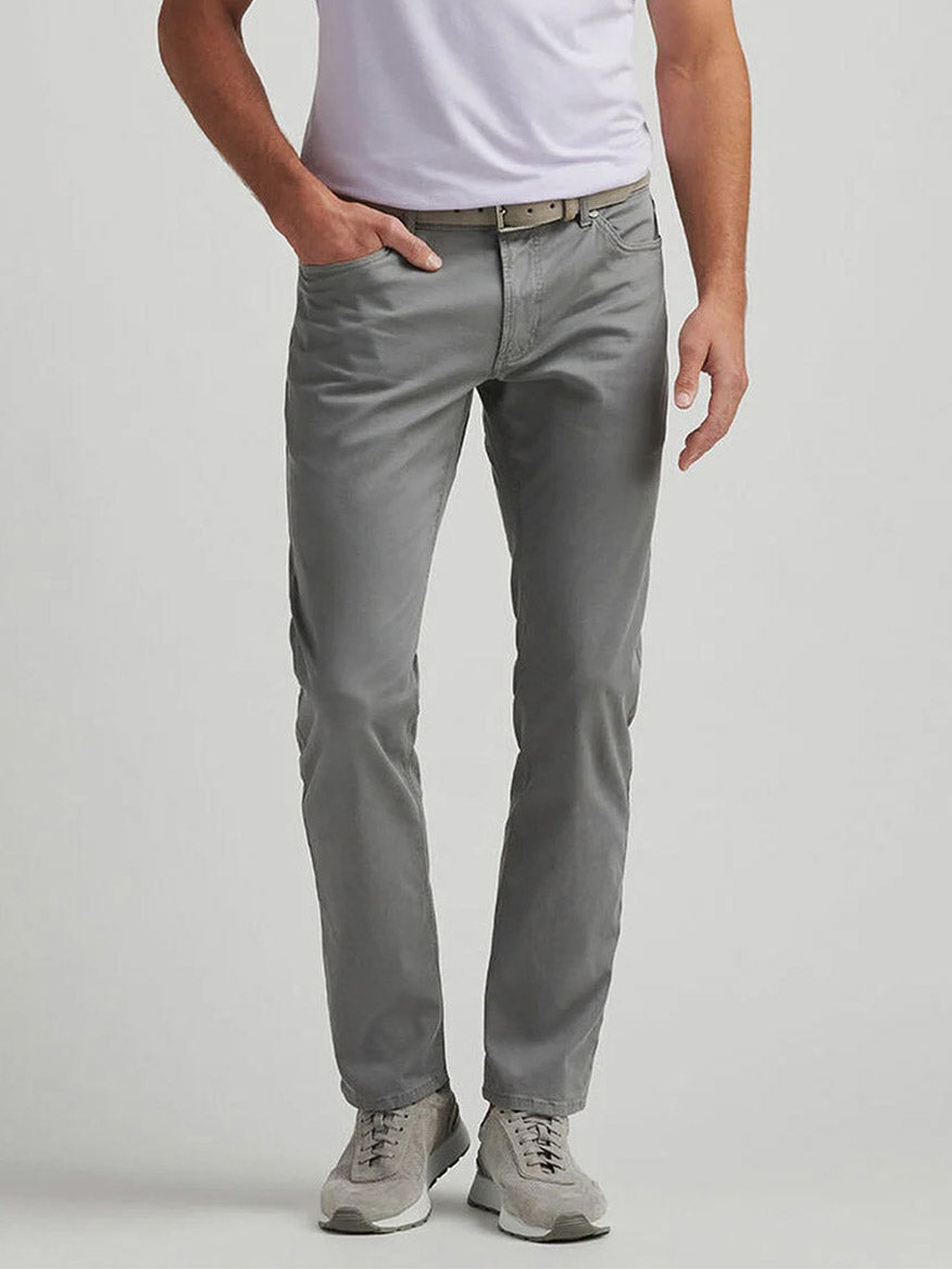 A person wears a white t-shirt and Peter Millar Wayfare Five-Pocket Pant in Classic Grey, paired with wrinkle-resistant light grey sneakers, standing against a plain background.