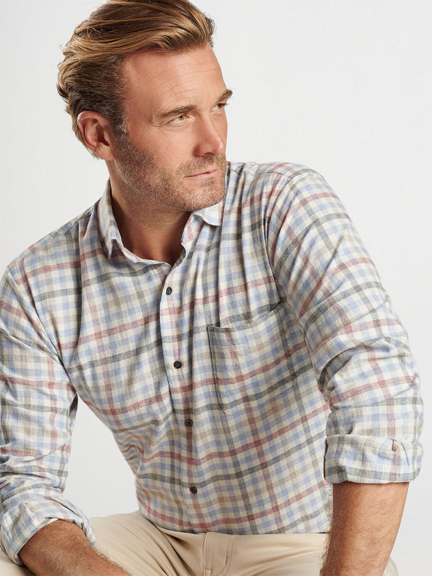 A man styled in the Peter Millar White Rock Cotton Sport Shirt in Winter Ivory, paired with beige pants. He gazes to the side against a simple backdrop, with his look accentuated by the shirt's spread collar.