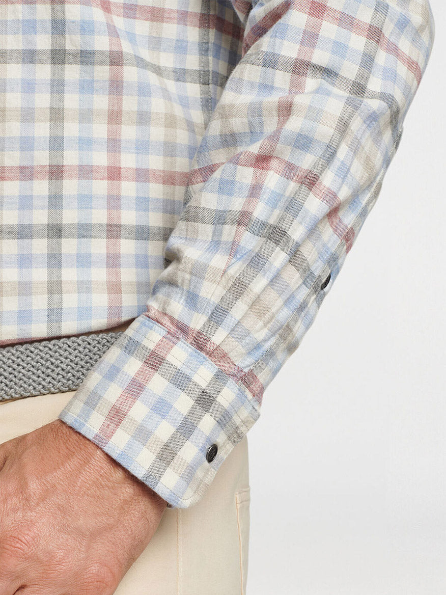 A close-up of someone wearing the Peter Millar White Rock Cotton Sport Shirt in Winter Ivory shows a classic fit with blue, red, and beige checks. Crafted from soft cotton twill, the shirt features a spread collar and visible right arm with its folded cuff and buttons. It’s paired with beige pants for a timeless look.