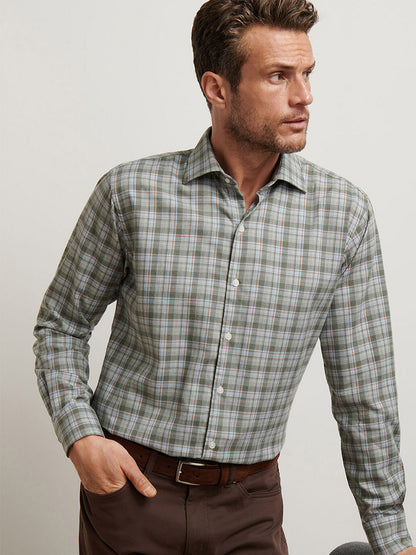 A man wearing the Peter Millar Whitecap Performance Flannel Sport Shirt in Basil and brown pants stands against a plain light-colored background, looking to his left.