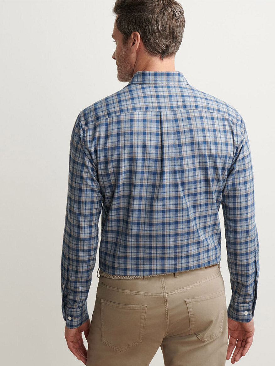 A man stands with his back to the camera, wearing a Peter Millar Whitecap Performance Flannel Sport Shirt in Blue Haze and light brown pants against a plain background.