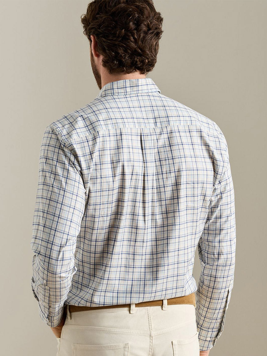 A man faces away, wearing the Peter Millar Wyatt Crown Soft Twill Sport Shirt in Multi—a blue and tan checkered shirt with elbow patches, crafted from easy-care stretch performance fabric—paired with cream-colored pants and standing against a plain background.