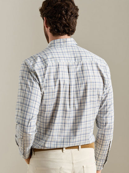 A man faces away, wearing the Peter Millar Wyatt Crown Soft Twill Sport Shirt in Multi—a blue and tan checkered shirt with elbow patches, crafted from easy-care stretch performance fabric—paired with cream-colored pants and standing against a plain background.
