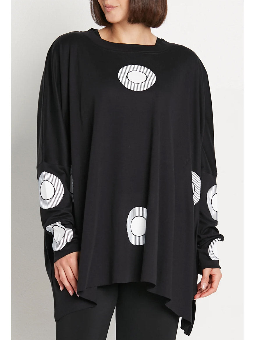 Person wearing a stylish Planet by Lauren G Spotlight Crew Swing Tee in Black/White, a loose, long-sleeved black top with white circular patterns on the front and sleeves.