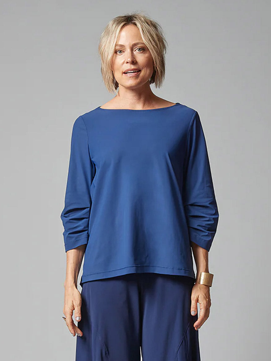 A woman wearing a travel-friendly Porto Eloise top in Atlantic with three-quarter sleeves and matching pants against a grey background.