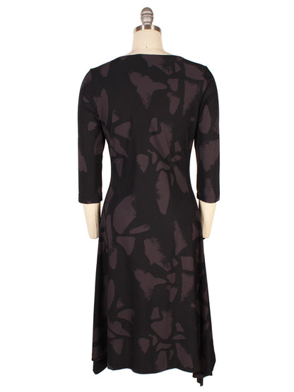 The Porto Risa Dress in Mulberry Palermo features 3/4 sleeves, an abstract dark gray pattern on black fabric, and an asymmetrical hem, shown from the back on a dress form. Made in Italy.