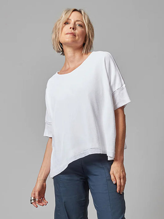 Woman in a Porto Tara Mesh Oversize Knit Top in White and blue trousers standing against a grey background.