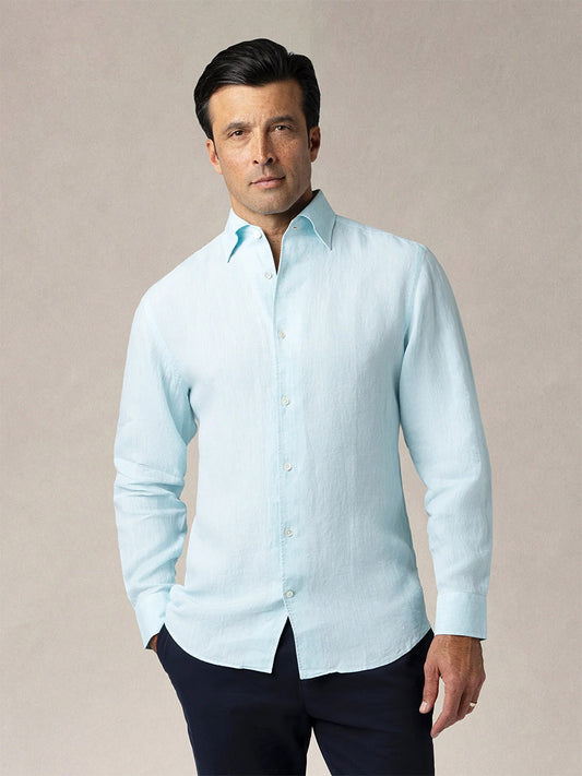 A man faces forward in a Robert Talbott Morgan Linen Shirt in Aqua, featuring a California One-Piece Collar, paired with dark pants against a plain neutral background.