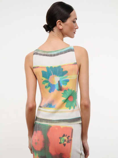 A woman with dark hair in a low bun wears the STAUD Bryn Top in Superbloom Scarf, a sleeveless piece featuring large, colorful, blurred floral prints with silver stud accents, standing against a plain white background.