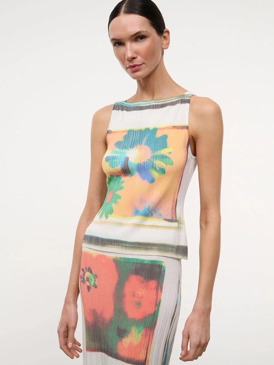 A woman wears the STAUD Bryn Top in Superbloom Scarf, a sleeveless piece with silver studs, paired with a matching colorful abstract floral skirt, standing against a plain white background.
