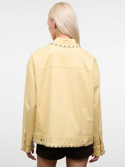 Person with long blonde hair wears the STAUD Clarke Jacket in Butter Studs, which has a boxy silhouette and metal stud details, shown from the back against a plain light background.