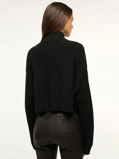 Woman with straight brown hair wears the STAUD Cropped Hampton Cashmere Sweater in Black, a long-sleeve, chunky knit style, paired with black leather pants, shown from the back against a plain white background.