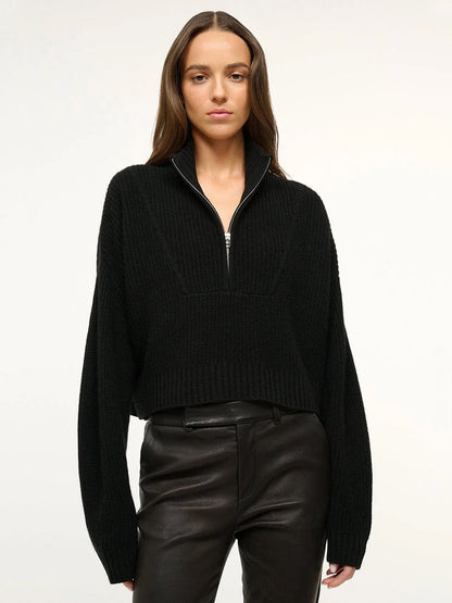 A woman wearing the STAUD Cropped Hampton Cashmere Sweater in Black and black leather pants stands against a plain light background.