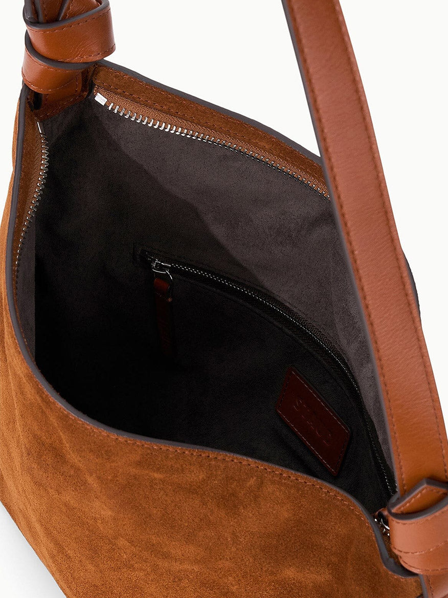 Close-up view of the STAUD Dani Shoulder Bag in Tabac, an open brown suede shoulder bag with leather straps and an asymmetrical silhouette, revealing a dark fabric interior lining and an inner zippered pocket.