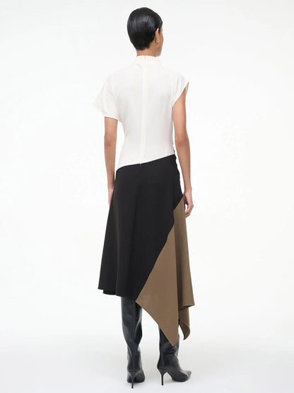 A person stands facing away, wearing the STAUD Davina Dress in Black Multi with a handkerchief hem, and black knee-high boots against a plain white background.