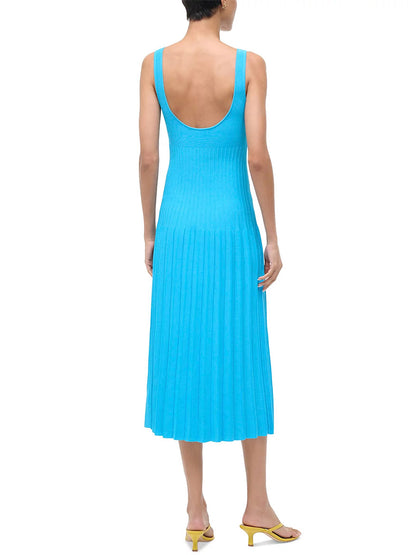 A person stands facing away, wearing the STAUD Ellison Sleeveless Dress in Pool—a bright blue compact knit dress with a flattering fit, scoop-back, pleated skirt—and yellow heeled sandals.