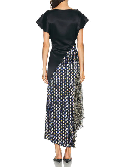 A woman stands facing away, wearing the STAUD Fawn Silk Dress in Black Multi—a black stretch silk dress with short sleeves, an asymmetrical skirt, and a pleated polka dot pattern.